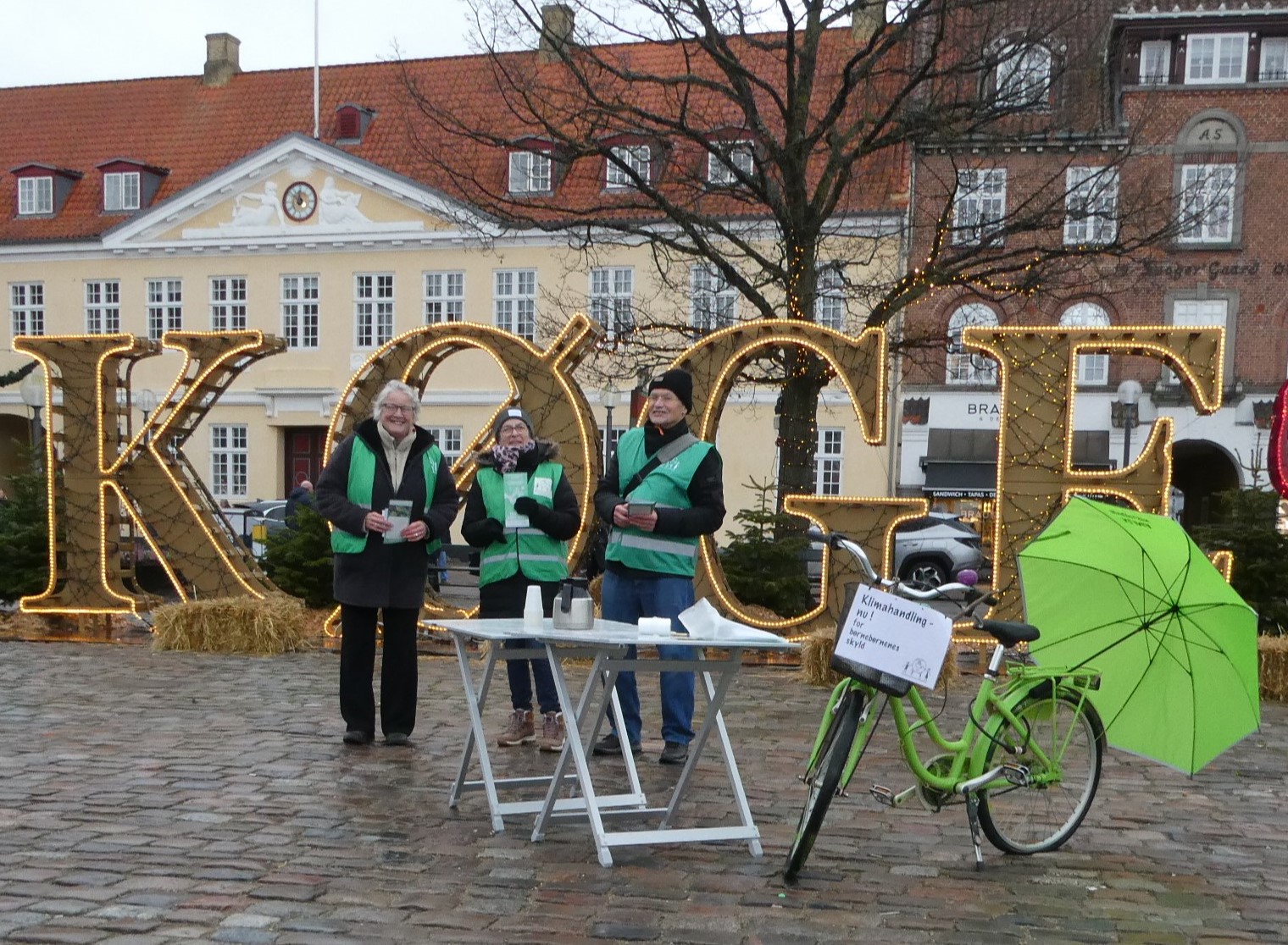 Tre bedsteforældre og en grøn cykel og grøn paraply på Køge Torv